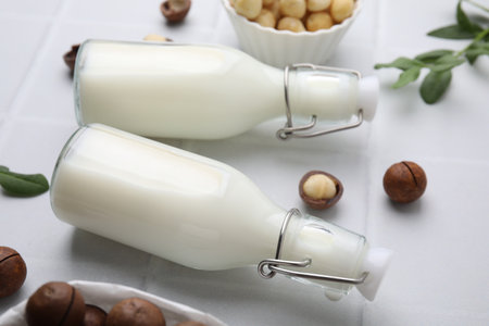Bottles of macadamia milk and nuts on white tiled table, closeupの写真素材