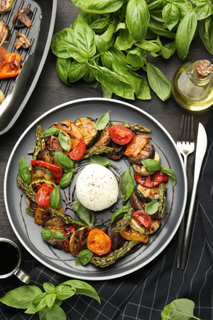 Tasty salad with grilled vegetables and mozzarella cheese served on black wooden table, flat layの写真素材