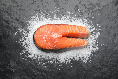 Fresh raw salmon steak with salt on dark textured table, above viewの写真素材