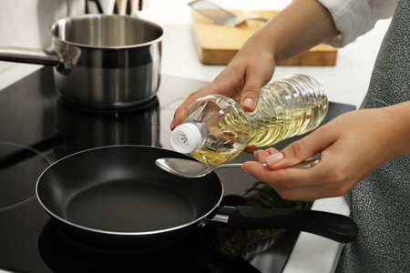 Woman with bottle of oil and spoon in kitchen, closeupの写真素材