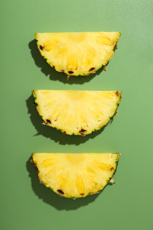 Slices of fresh pineapple on green background, flat layの写真素材