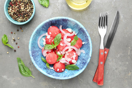 Delicious watermelon salad with feta cheese, mint and onion in bowl served on gray textured table, flat layの写真素材