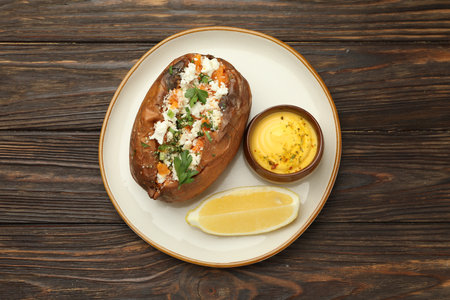 Tasty baked sweet potato with feta cheese, parsley, sauce and lemon slice on wooden table, top viewの写真素材