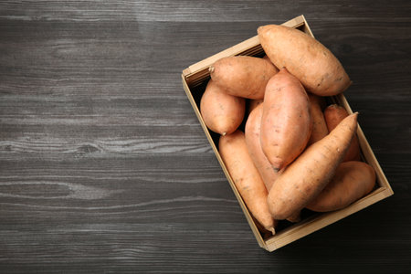 Fresh raw sweet potatoes in crate on wooden table, top view. Space for textの写真素材