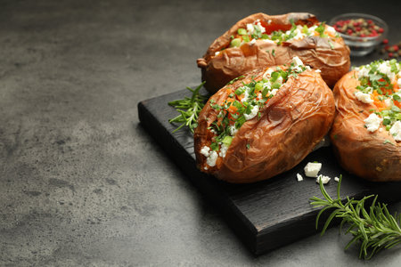 Tasty cooked sweet potatoes with feta cheese, green onion, parsley and rosemary on gray textured table, closeup. Space for textの写真素材