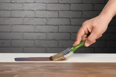 Man with brush applying walnut wood stain onto wooden surface, closeupの写真素材