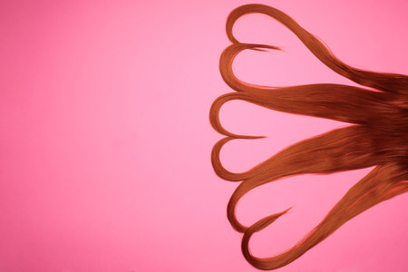 Red hair strands in shape of hearts on pink background, top view. Space for textの写真素材