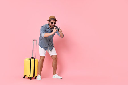 Happy man with vintage camera and suitcase on pink background, space for textの写真素材