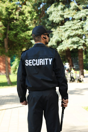 Security guard in uniform with baton outdoors, back view