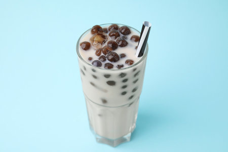 Tasty milk bubble tea in glass on light blue background, closeup