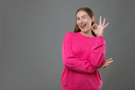 Smiling girl with braces showing ok gesture on grey background, space for textの写真素材