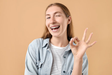 Smiling girl with braces showing ok gesture on beige backgroundの写真素材