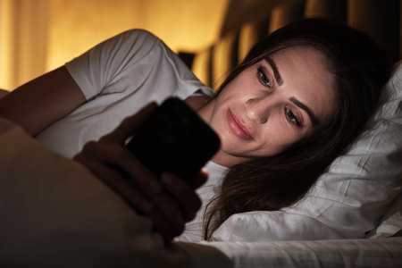 Bad habit. Young woman using smartphone in bed at nightの写真素材