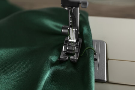 Sewing machine with green fabric on light background, closeup