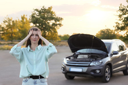Stressed woman standing near broken car outdoors