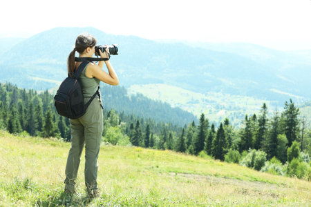 Photographer with backpack and camera taking picture of beautiful mountains, back view. Space for textの写真素材