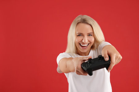 Person playing video games with controller on red background, space for text
