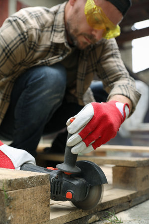Man grinding wooden planks with angle grinder outdoors, selective focusの写真素材