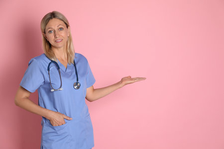 Portrait of doctor in medical uniform with stethoscope on pink background, space for textの写真素材