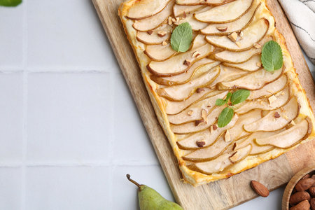 Delicious puff pastry tart with pears, almond and mint on light tiled table, flat lay. Space for textの写真素材