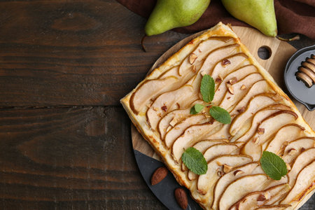 Delicious puff pastry tart with pears, almond and mint on wooden table, flat lay. Space for textの写真素材