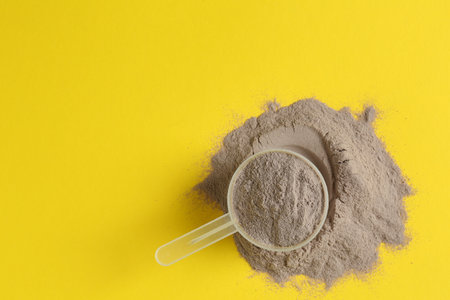 Protein powder and scoop on yellow background, top view. Space for textの写真素材