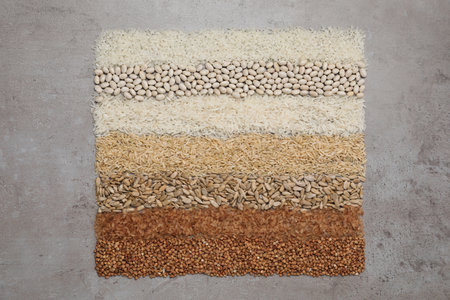 Different types of cereals, legumes and seeds on gray textured table, flat lay