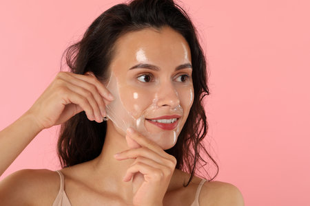 Smiling woman peeling off face mask on pink backgroundの写真素材