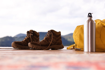 Trekking shoes, backpack and thermos on wooden tableの写真素材