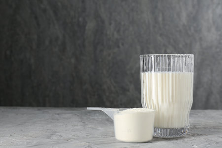 Delicious protein shake in glass and scoop with powder on gray textured table, space for textの写真素材