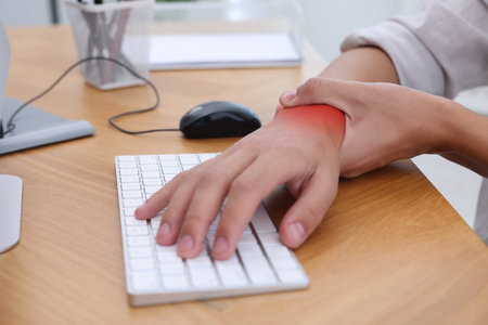 Man suffering from pain in wrist at wooden table, closeup. Office work, Carpal tunnel syndromeの写真素材