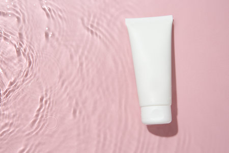 Cosmetic product. Tube with cream in water on pink background, top view. Space for textの写真素材