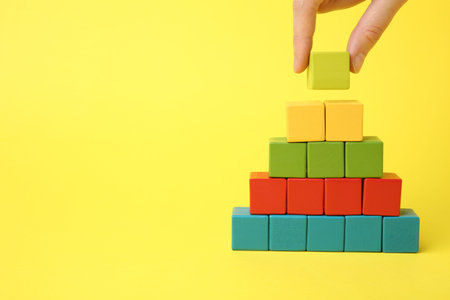 Woman building pyramid of cubes on yellow background, closeup. space for textの写真素材
