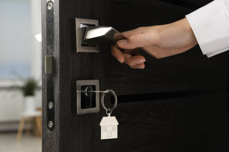 Woman opening door with key and house shaped keychain, closeup