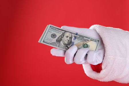 Santa Claus holding dollar banknotes on red background, closeup. Space for textの写真素材