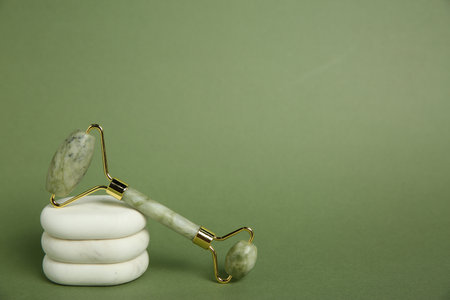 Face roller and massage stones on green background. Space for textの写真素材