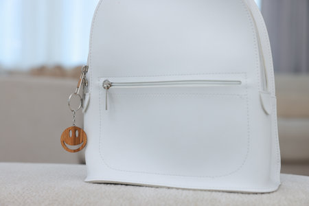 Stylish backpack with wooden keychain in shape of smiley face on soft surface indoors, closeupの写真素材