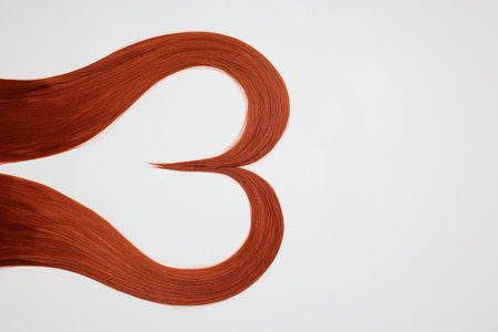 Red hair strands in the shape of heart on white background, top view. Space for text