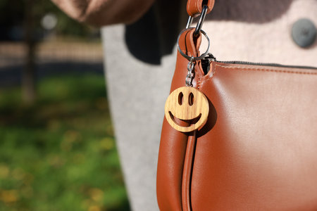 Woman with wooden keychain in shape of smiley face on her bag outdoors, closeupの写真素材