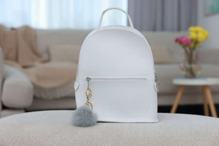 Stylish backpack with faux fur keychain on soft surface indoors