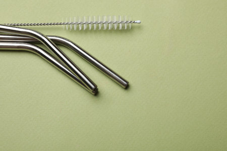Metal drinking straws and cleaning brush on green background, top view. Space for textの写真素材