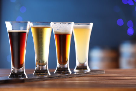 Glasses with different types of beer on wooden table against blue background, closeupの写真素材