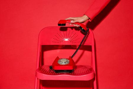 Woman with corded telephone on chair against red background, closeupの写真素材