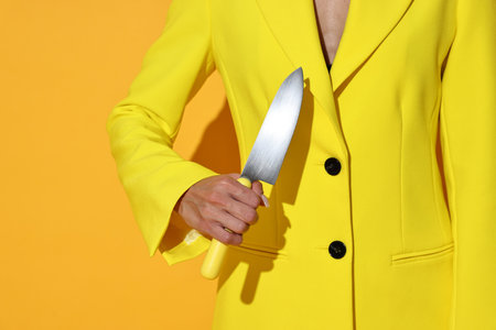 Woman with sharp knife on yellow background, closeupの写真素材