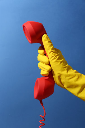 Woman in rubber glove holding red telephone handset on blue background, closeupの写真素材