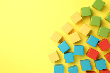 Many wooden colorful cubes on yellow background, flat lay. Space for text