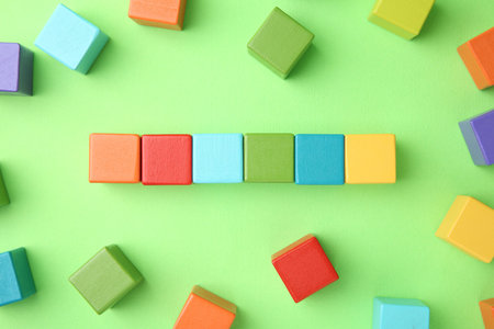 Many wooden colorful cubes on green background, top view