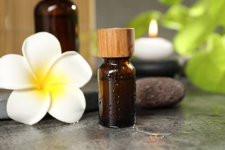 Spa composition with bottles of cosmetic products, plumeria flower and burning candle on gray table, closeupの写真素材
