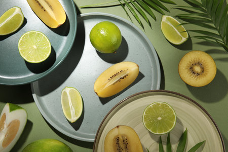 Pieces of delicious exotic fruits served on green table, flat lay