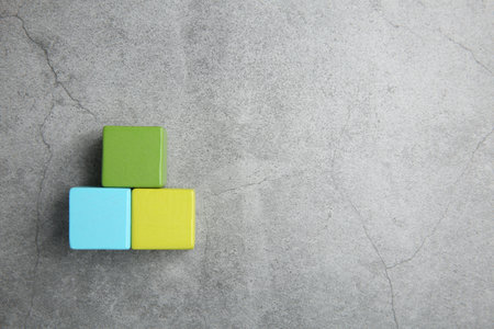 Pyramid of colorful cubes on gray textured background, top view. Space for text